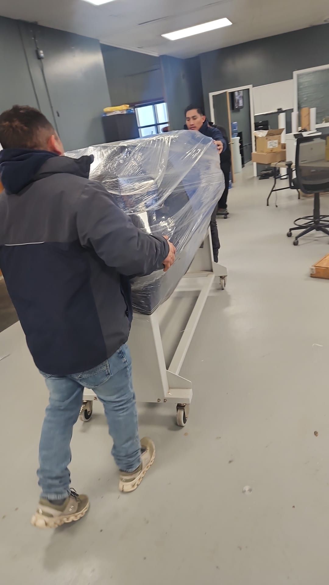 A man is carrying a large object on a cart in a room.
