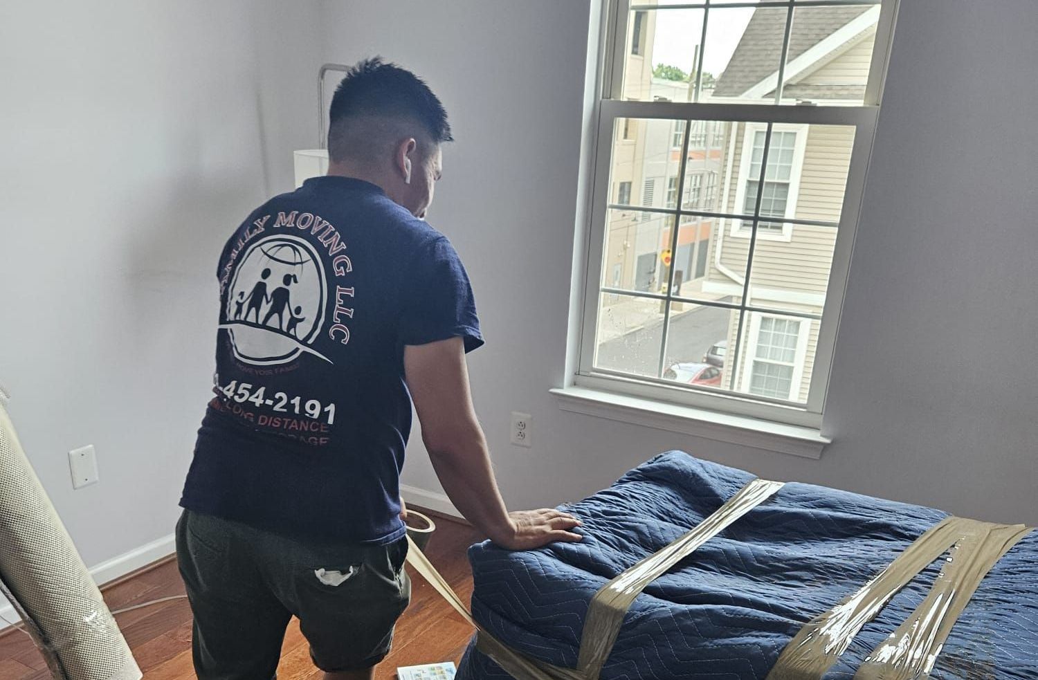 A man in a blue shirt is standing next to a bed in a room.