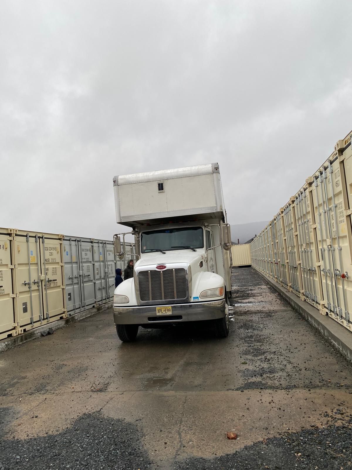 A white truck is parked next to a row of shipping containers.