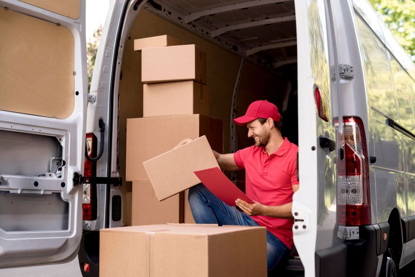 A delivery man is sitting in the back of a van filled with boxes.