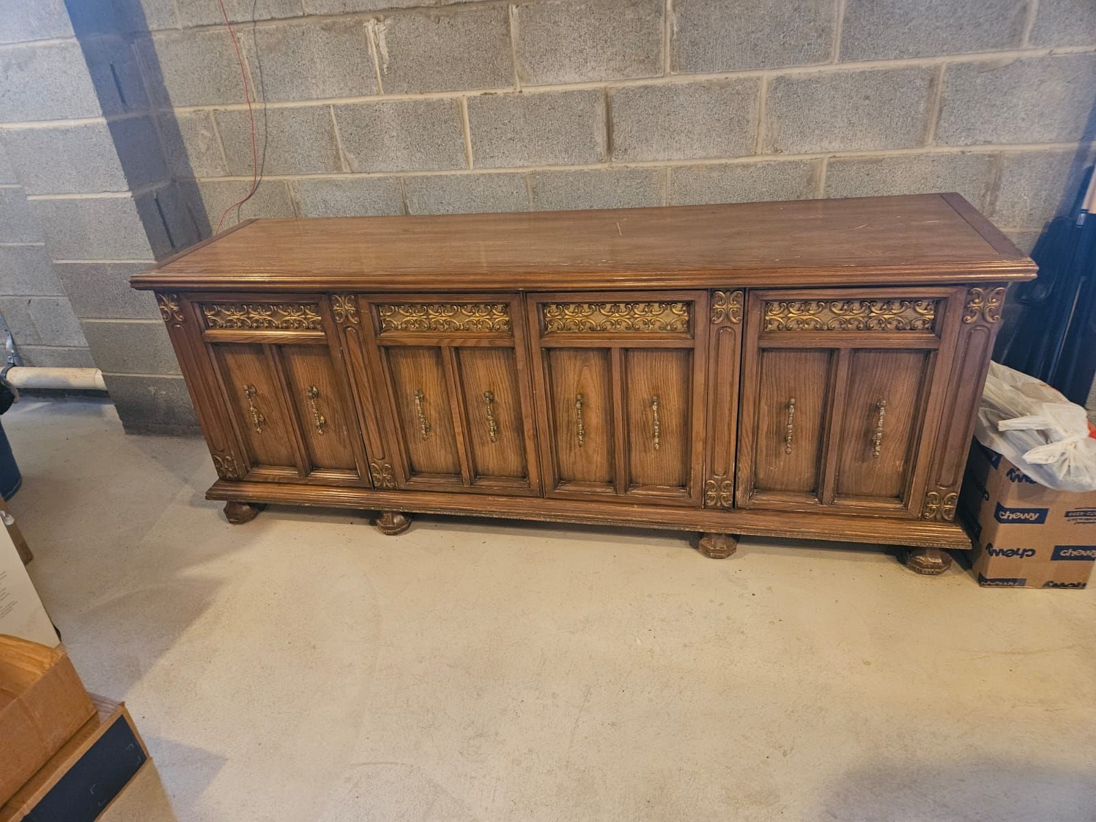 A wooden dresser is sitting on the floor in front of a brick wall.