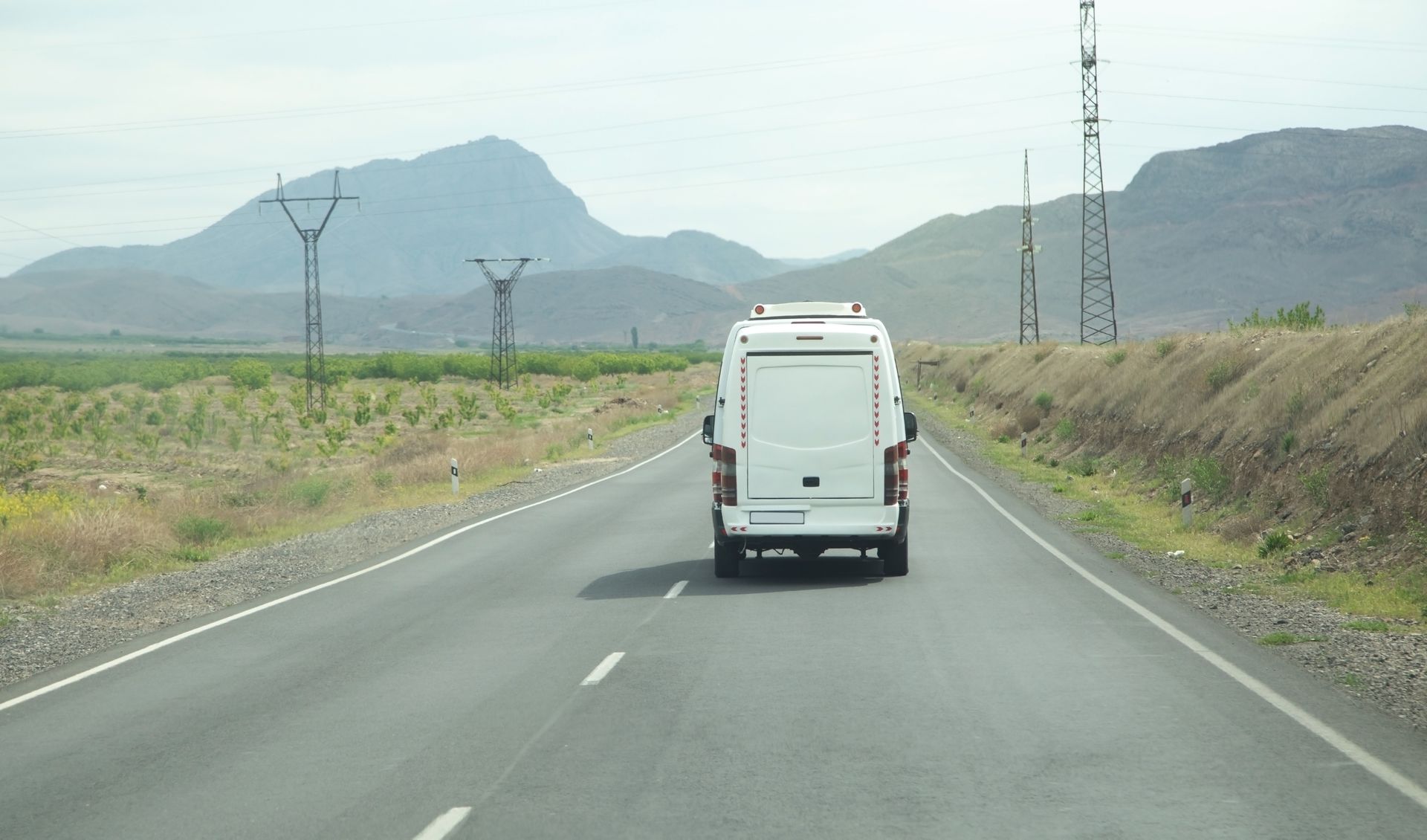 A white van is driving down a road with mountains in the background