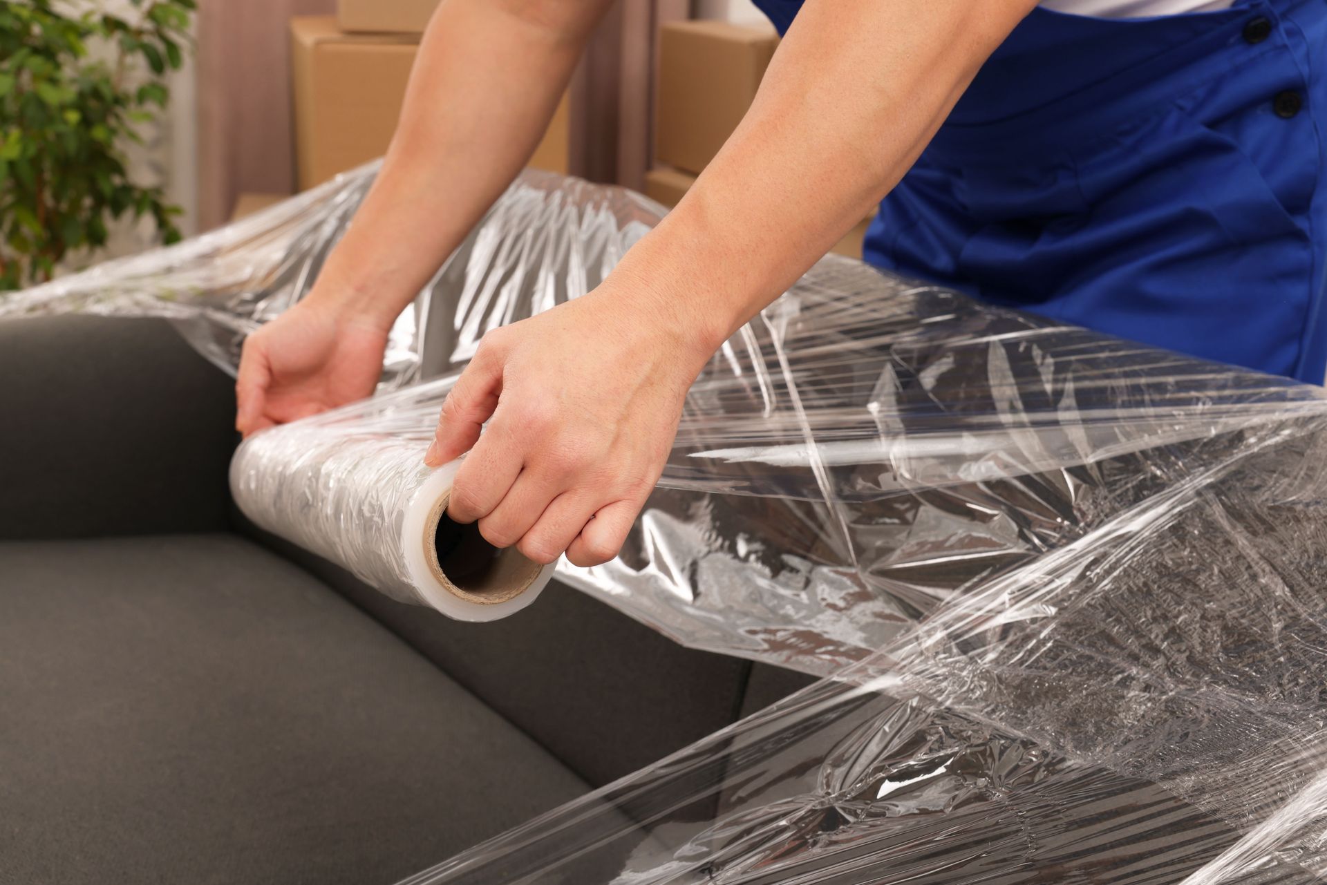 A person is wrapping a couch with plastic wrap.