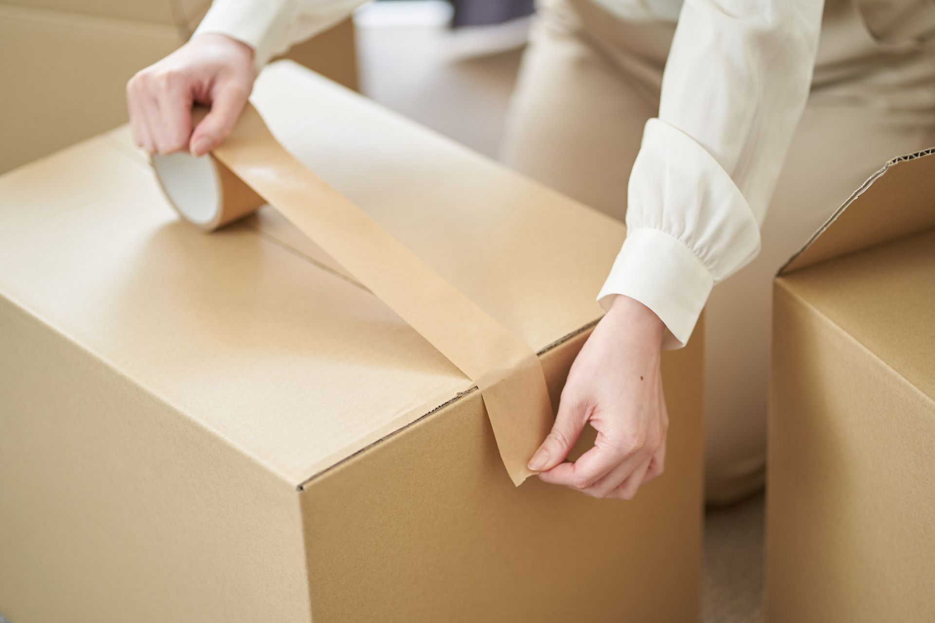 A woman is taping a cardboard box with tape.