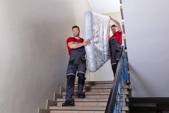 Two men are carrying a mattress up a set of stairs.