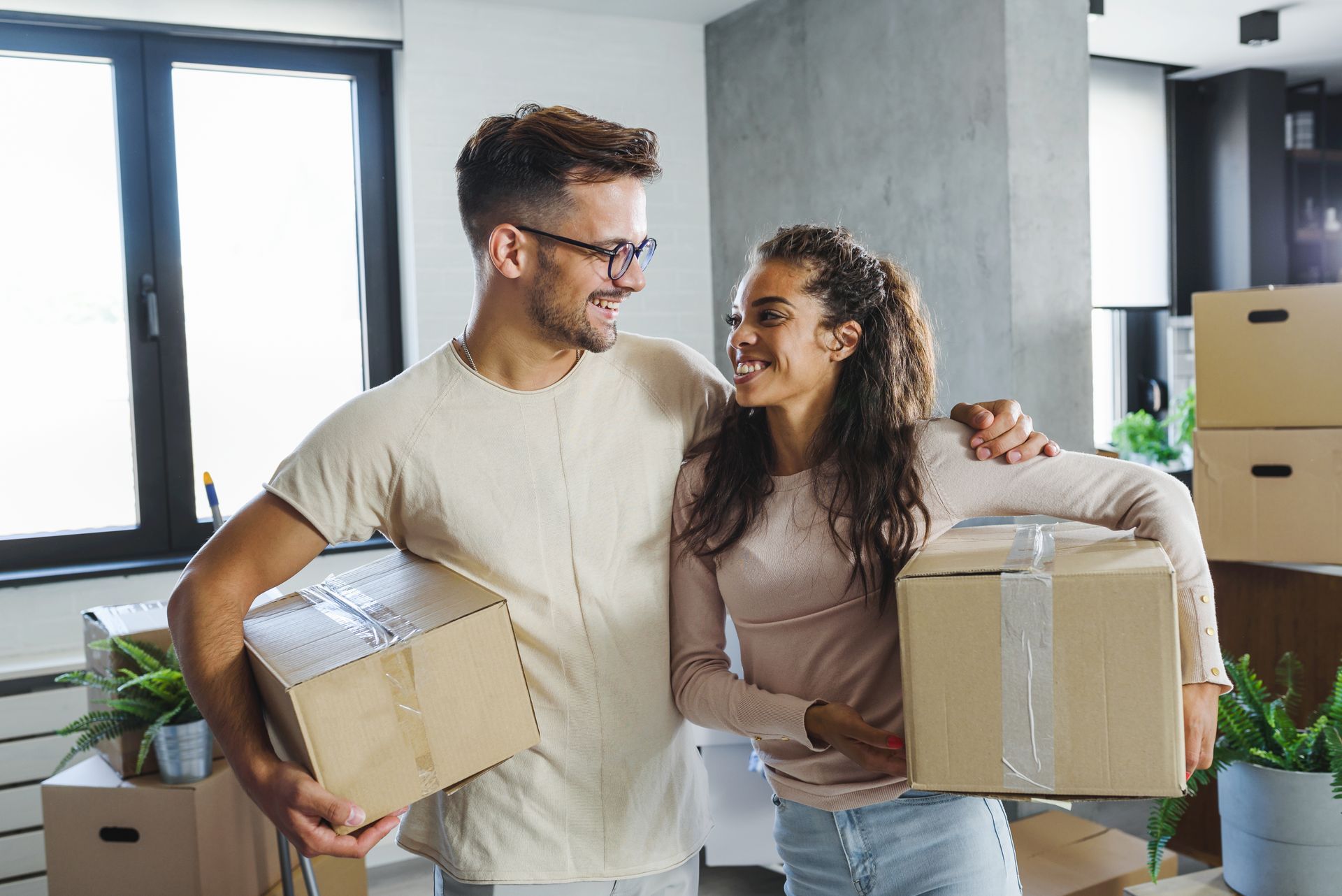 A man and a woman are holding cardboard boxes in their new home.