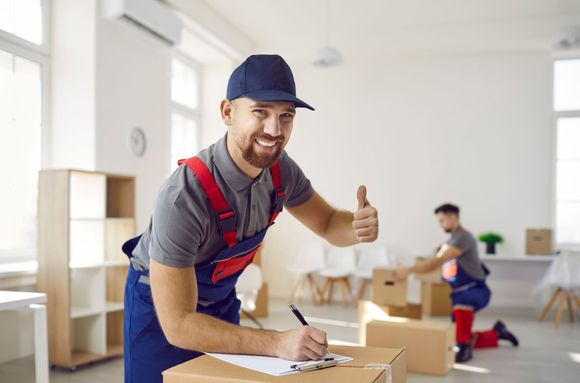 A man is giving a thumbs up while standing next to a box in a room.