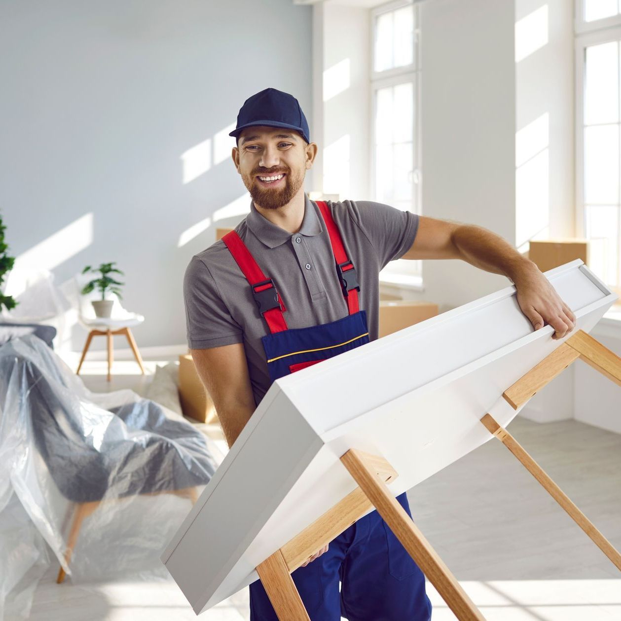 A man in overalls is holding a white table in a room.