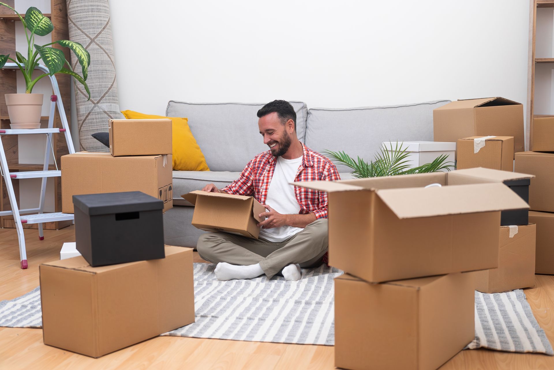 A man is sitting on the floor in a living room surrounded by cardboard boxes.