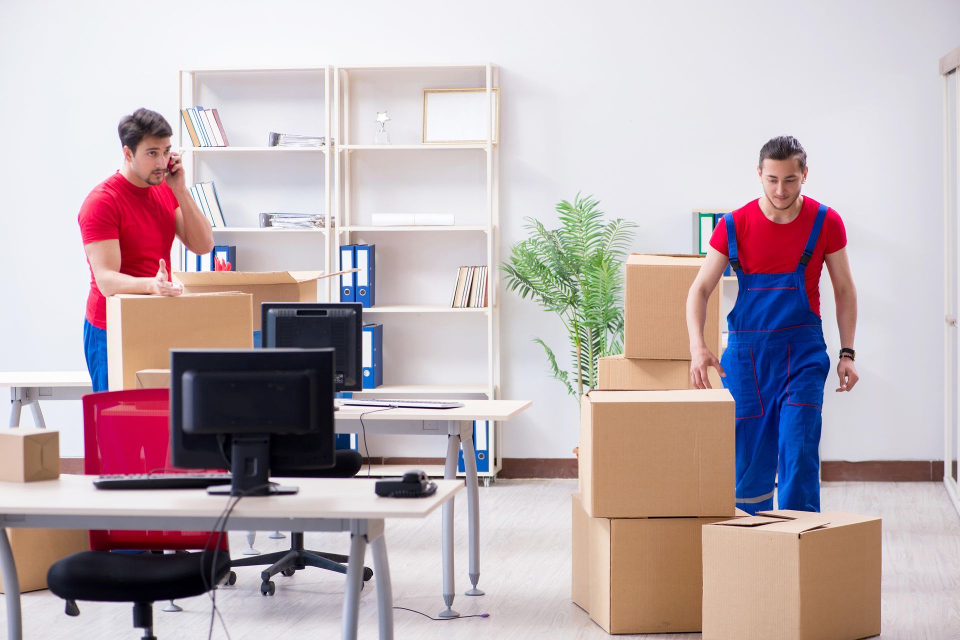 Two men are moving boxes in an office.