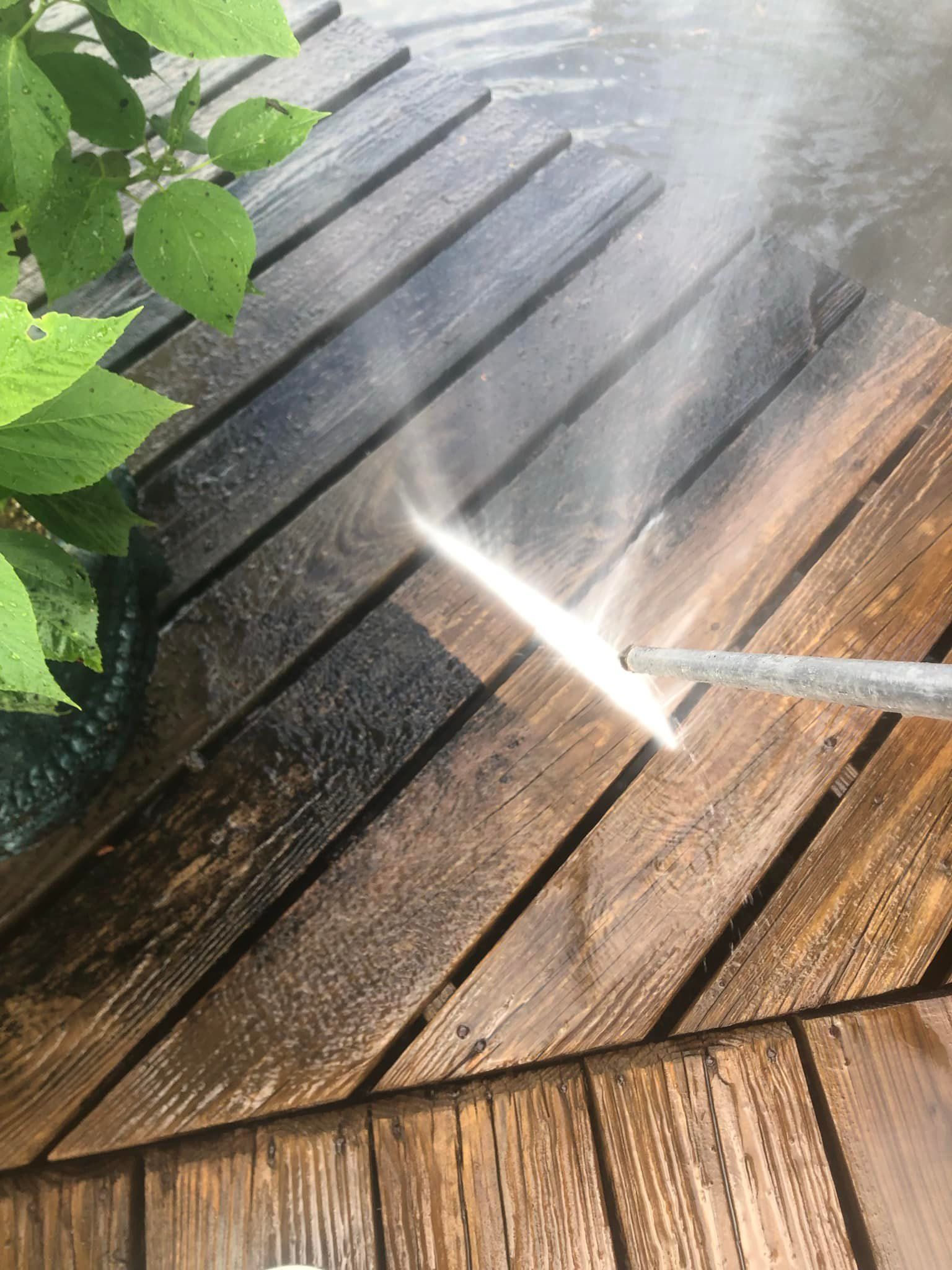 A person is using a high pressure washer to clean a wooden deck.