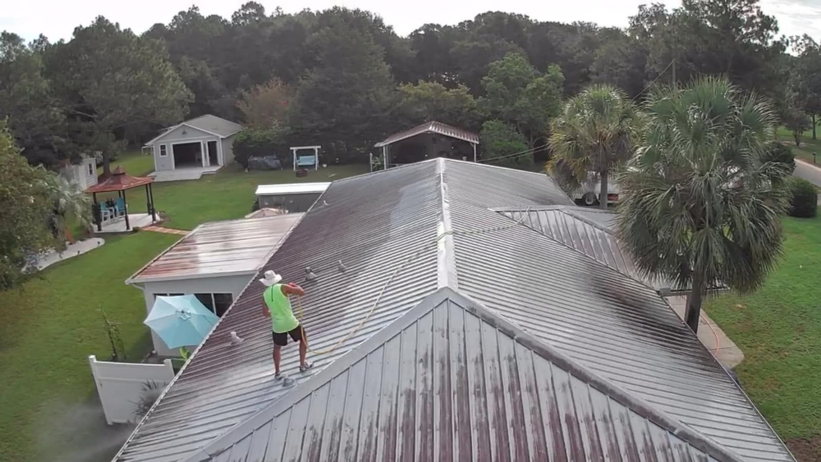A man is standing and cleaning the roof of a house.
