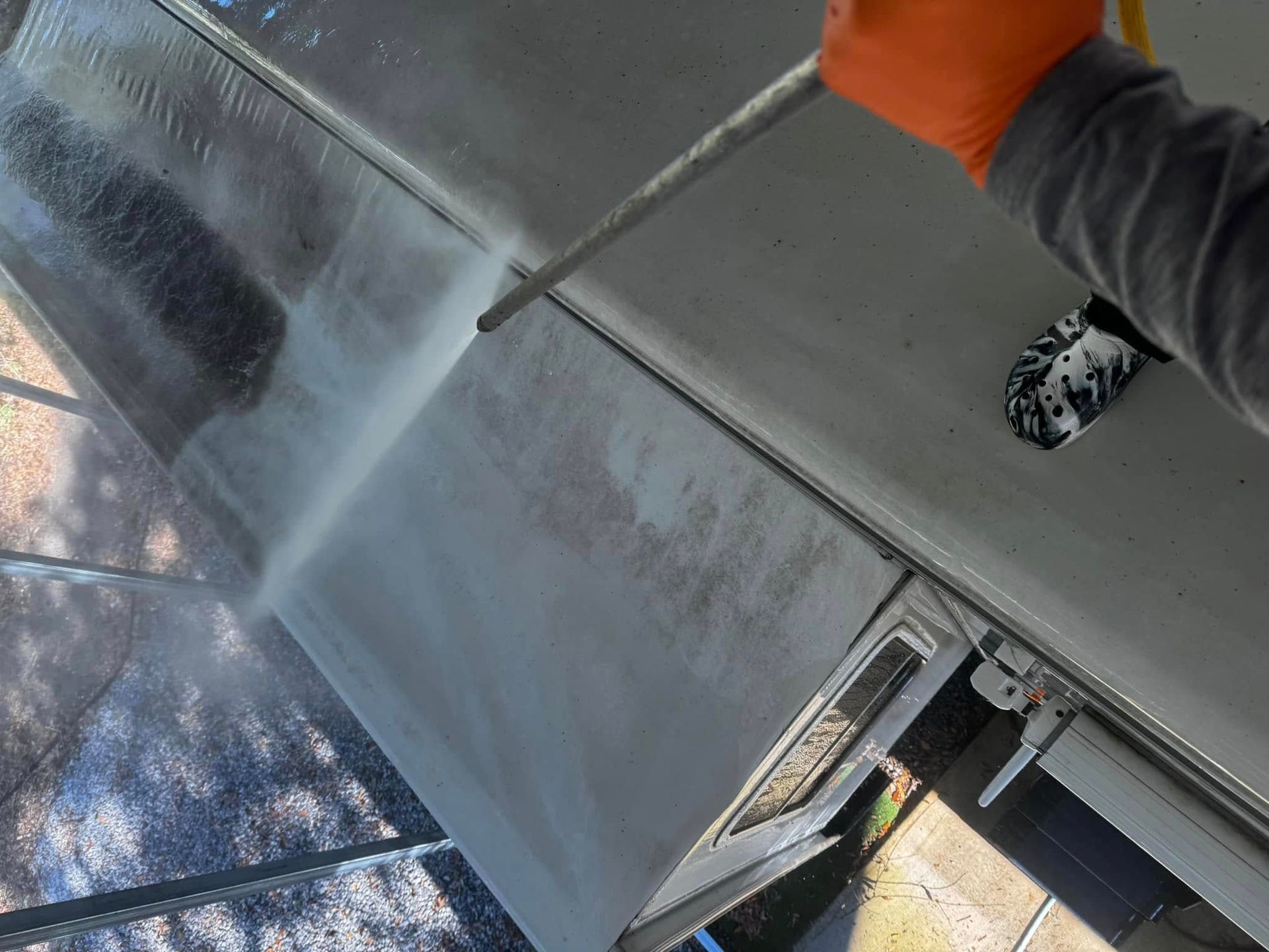 A person wearing orange gloves is cleaning a roof with a high-pressure washer.