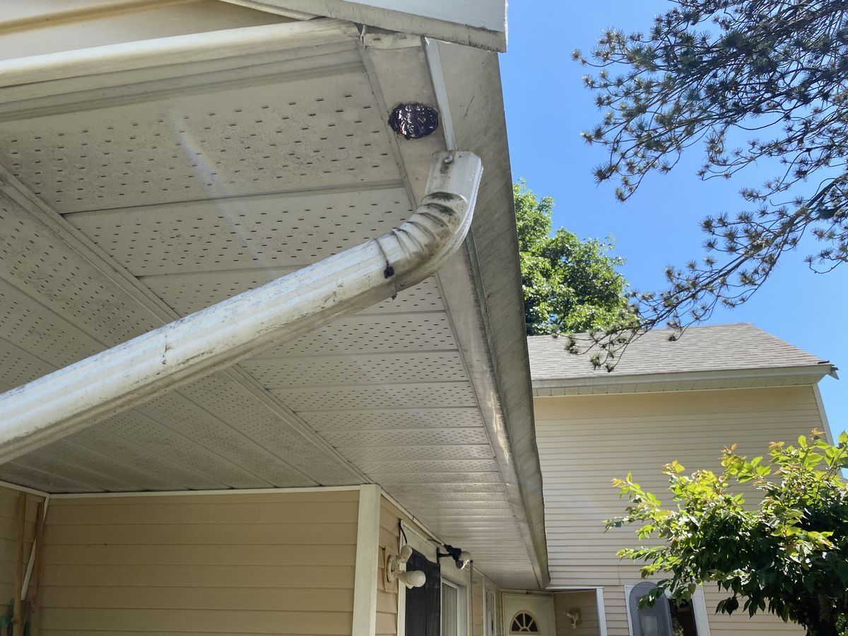 A white gutter is hanging from the roof of a house.