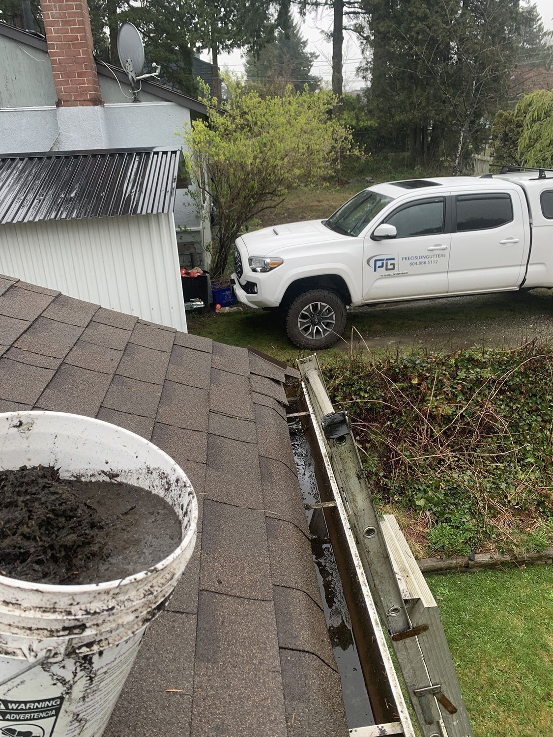 A white truck is parked on the side of a house next to a gutter.