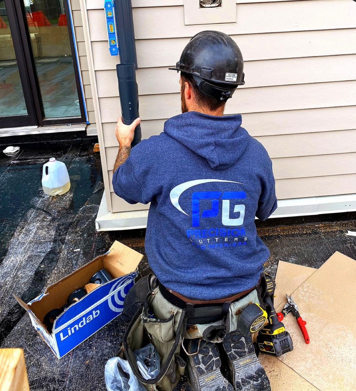 A man wearing a hard hat and a blue shirt with the letter t on the back