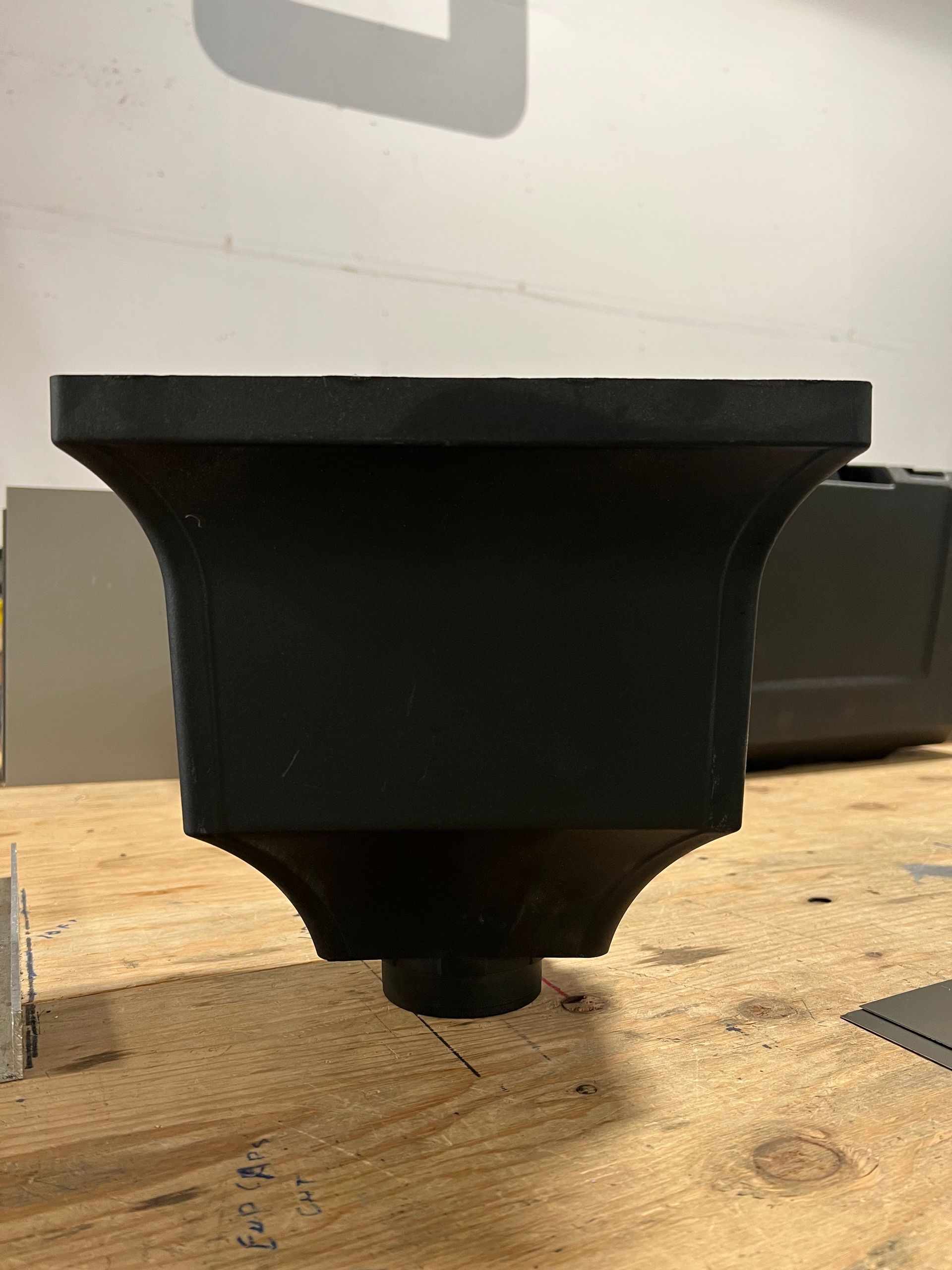 A black planter is sitting on top of a wooden table.