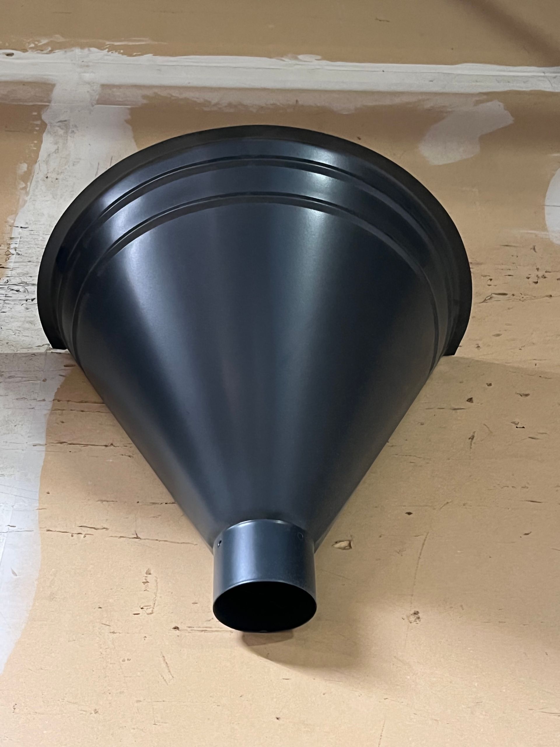 A black metal funnel is hanging on a wall.