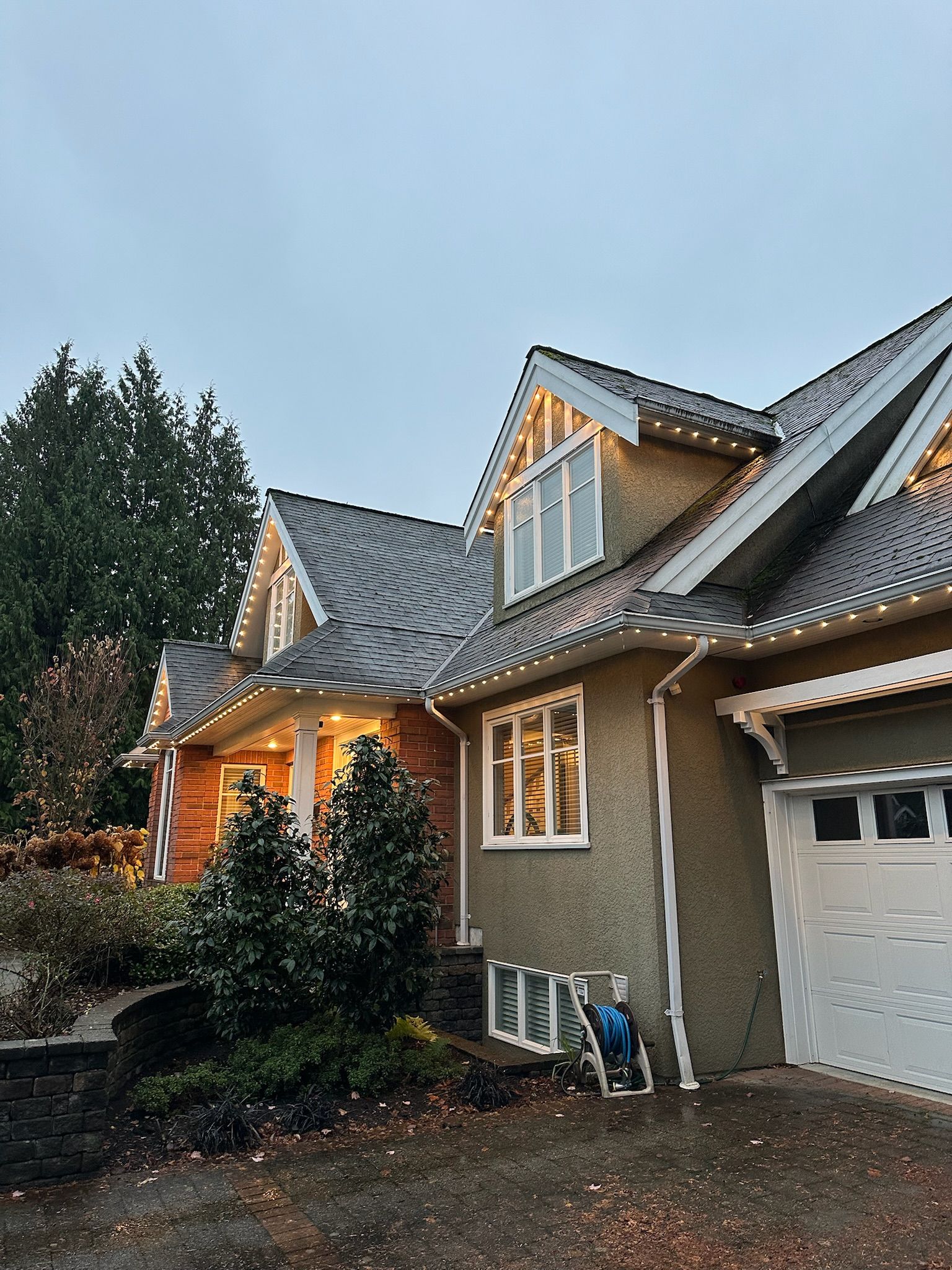 A large house with a garage and christmas lights on the roof.