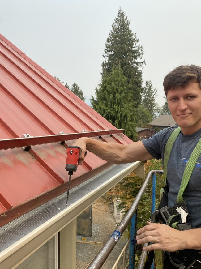 A man is working on a red roof with a drill.
