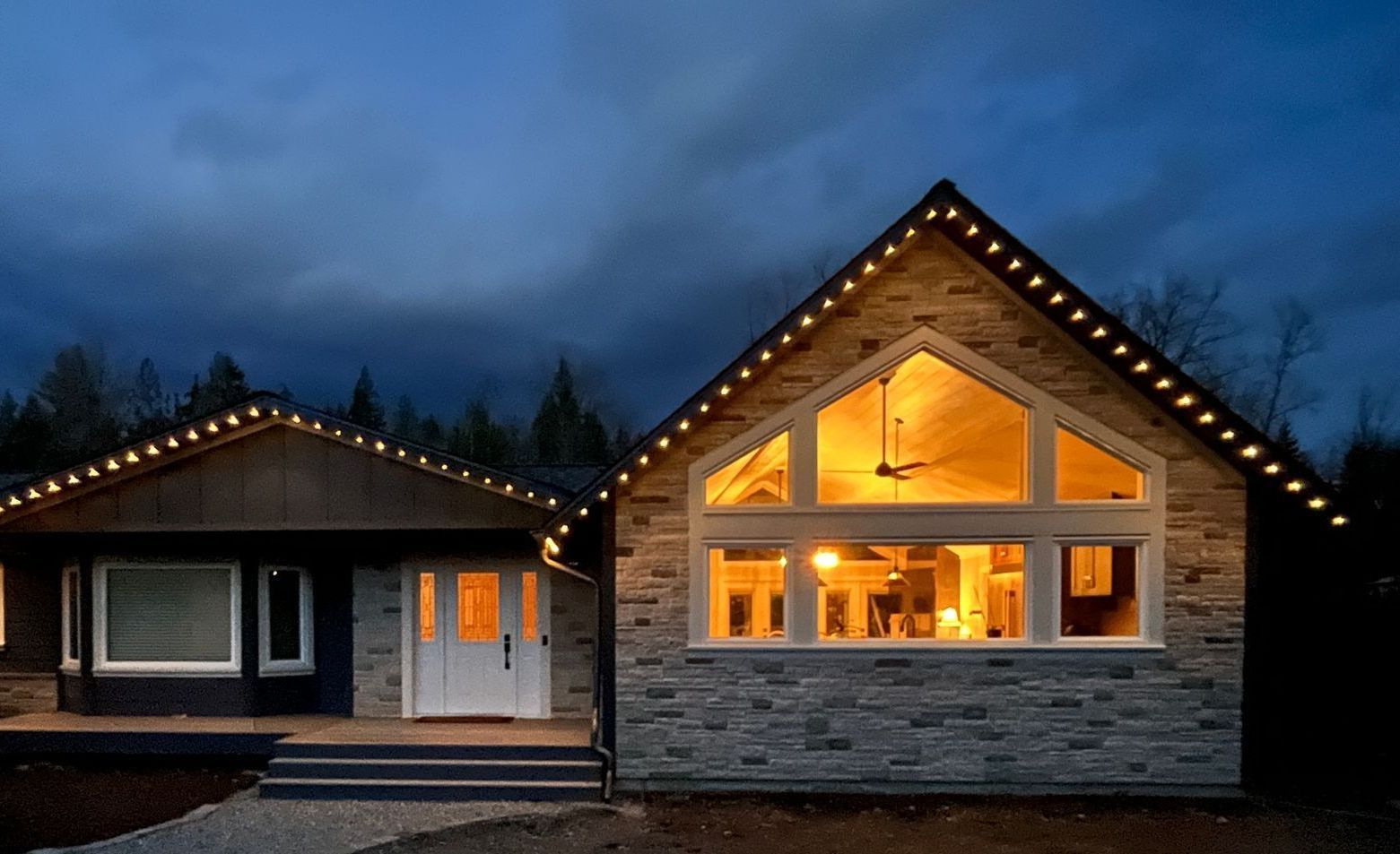 A house with christmas lights on the roof is lit up at night