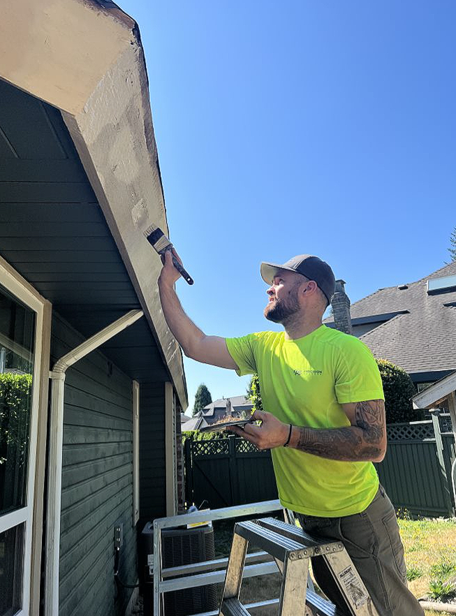 A man is painting the side of a house with a brush.
