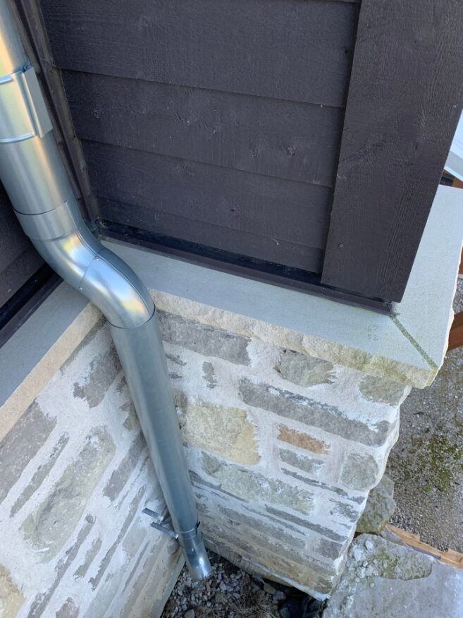 A metal gutter is attached to the side of a stone wall.