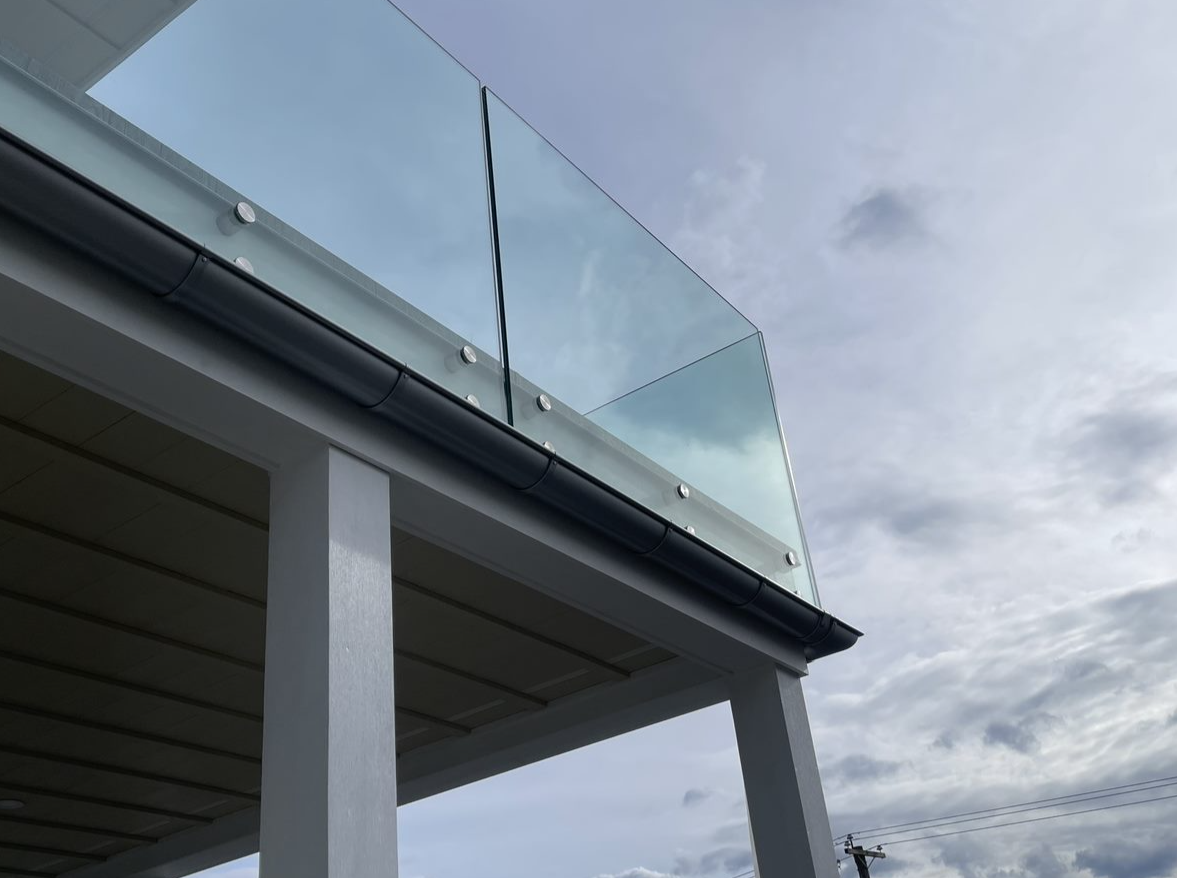 A balcony with a clear glass railing against a cloudy sky