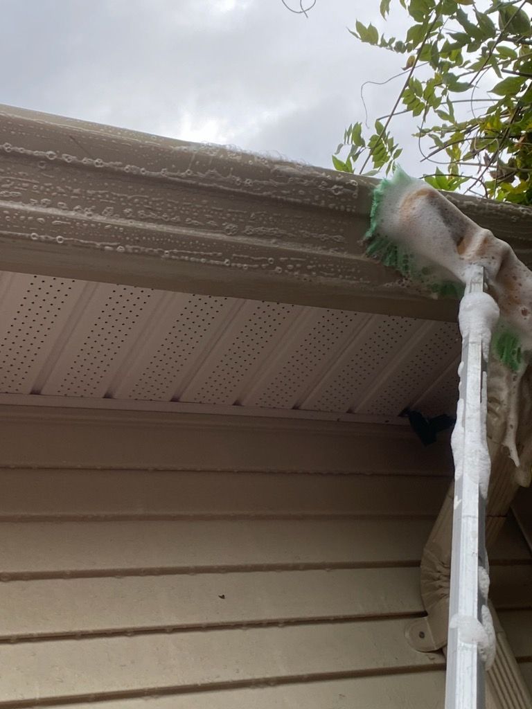 A person is cleaning the gutters of a house with a brush.
