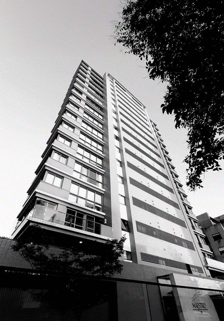 Prédio alto e moderno, visto de um ângulo baixo, com muitas janelas, contra um céu claro.