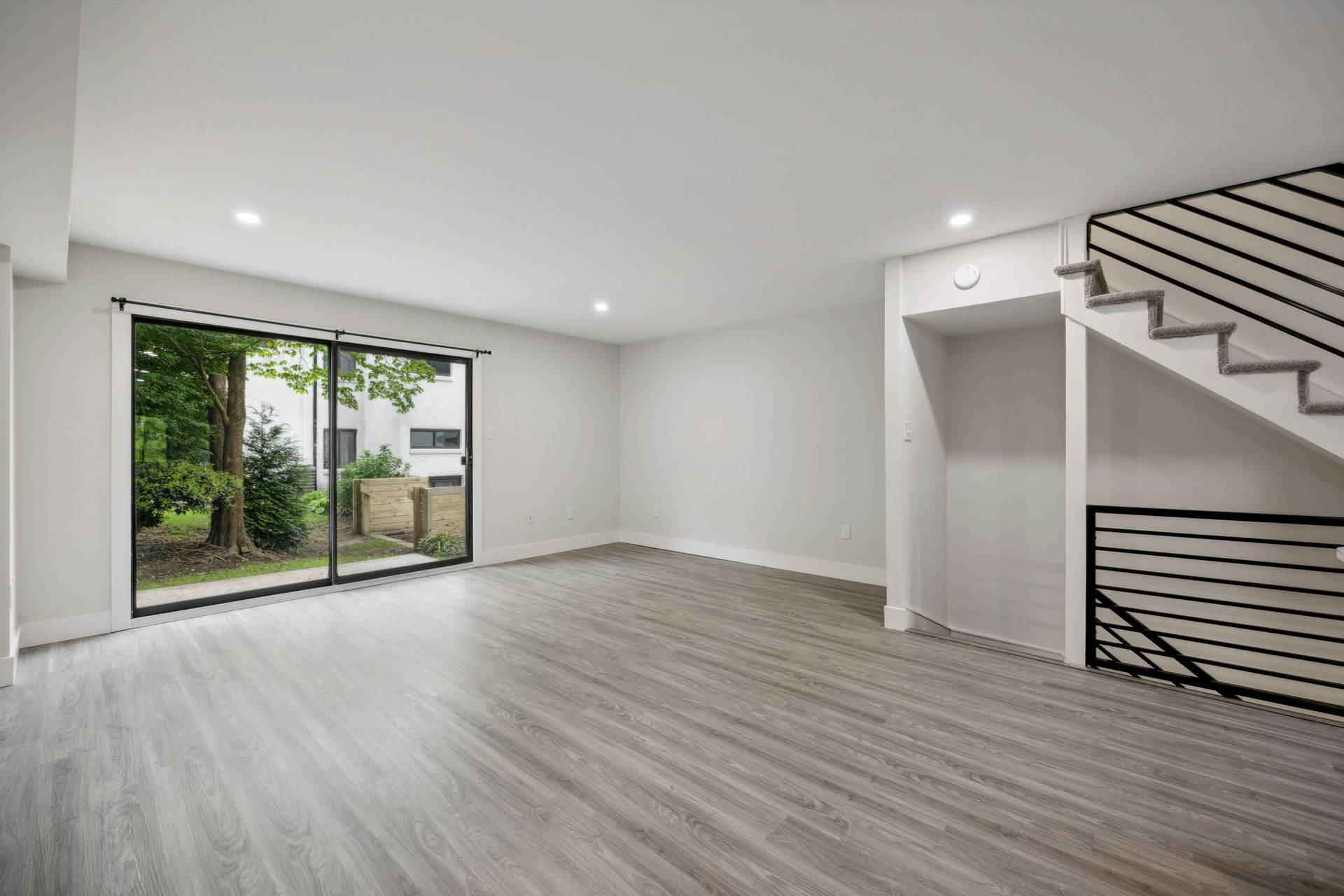 Empty room with light gray flooring and white walls, sliding glass door, and stairs.