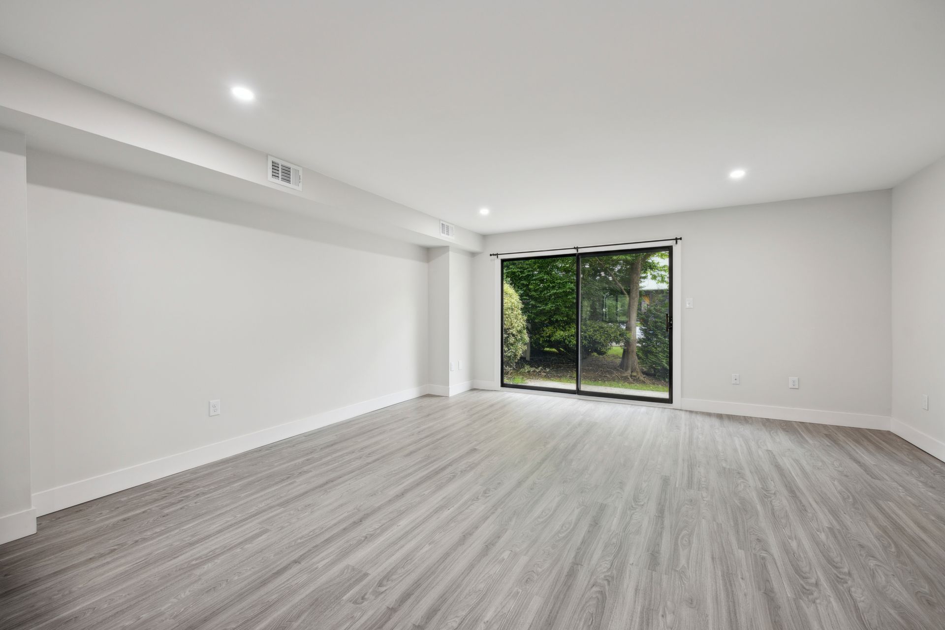 Empty room with gray wood-look flooring, white walls and ceiling, and a large sliding glass door.
