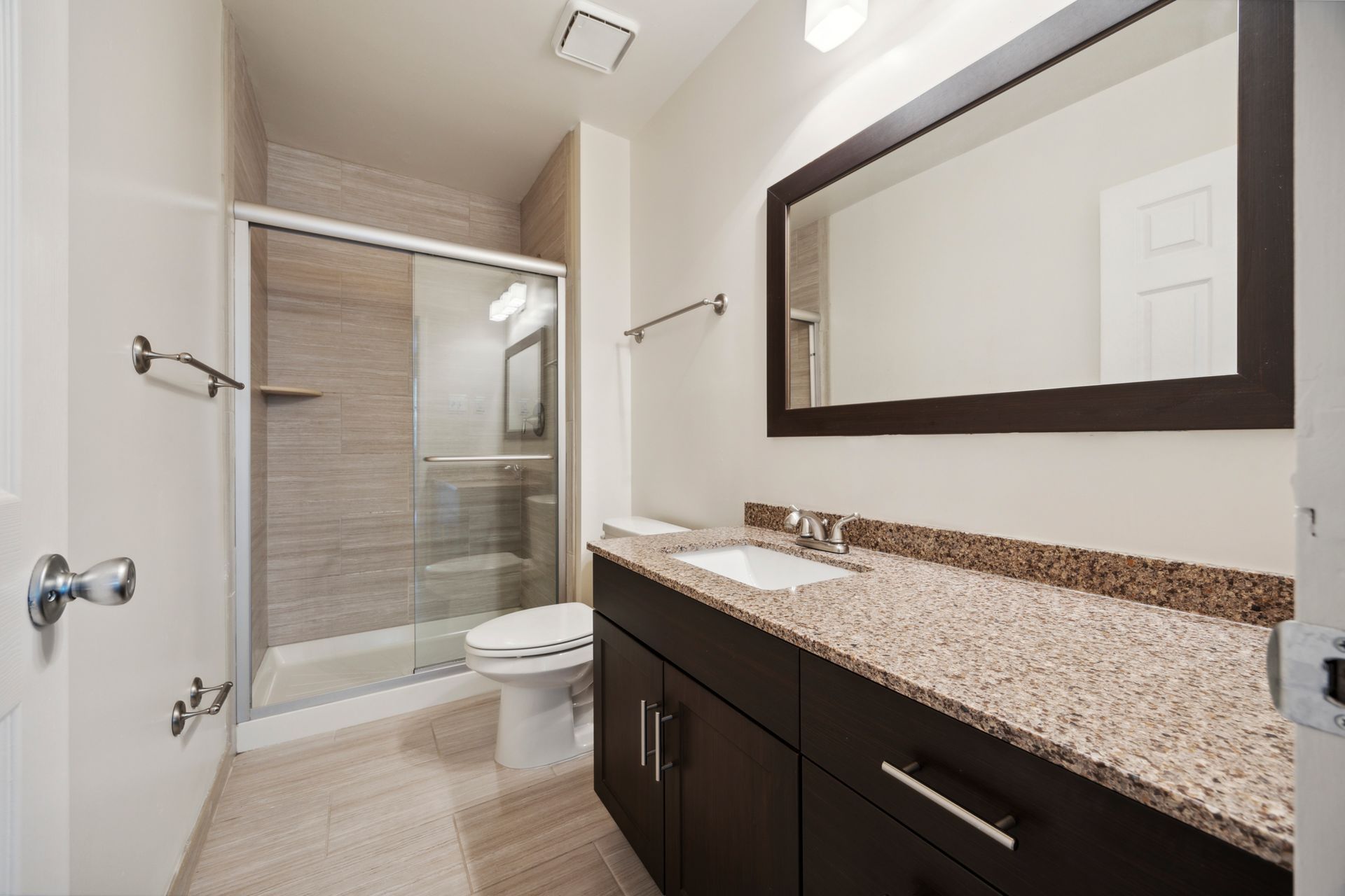 Modern bathroom with a glass shower, dark vanity, and large mirror.