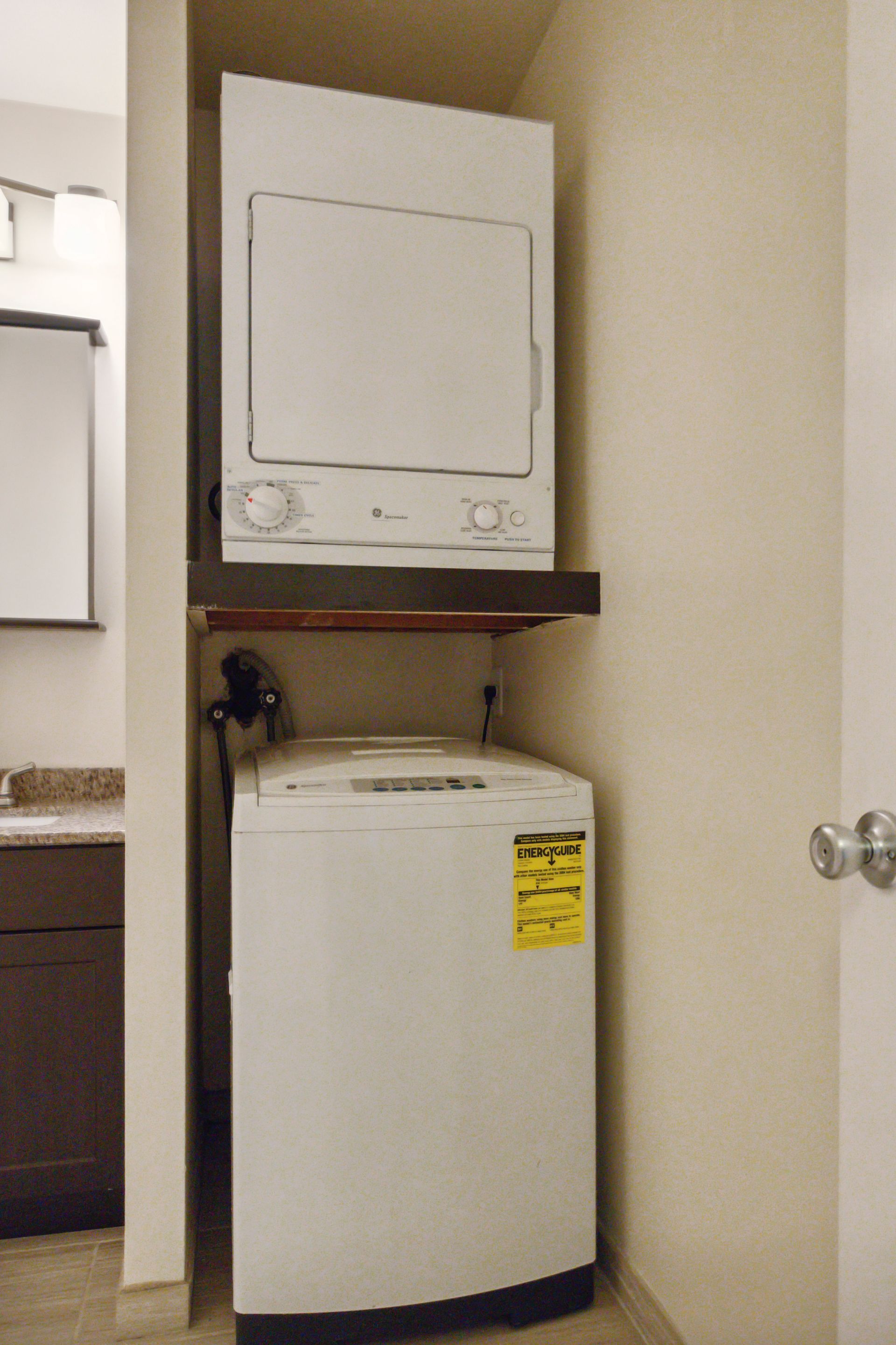 Stacked white washer and dryer in a small alcove; top unit is a dryer.