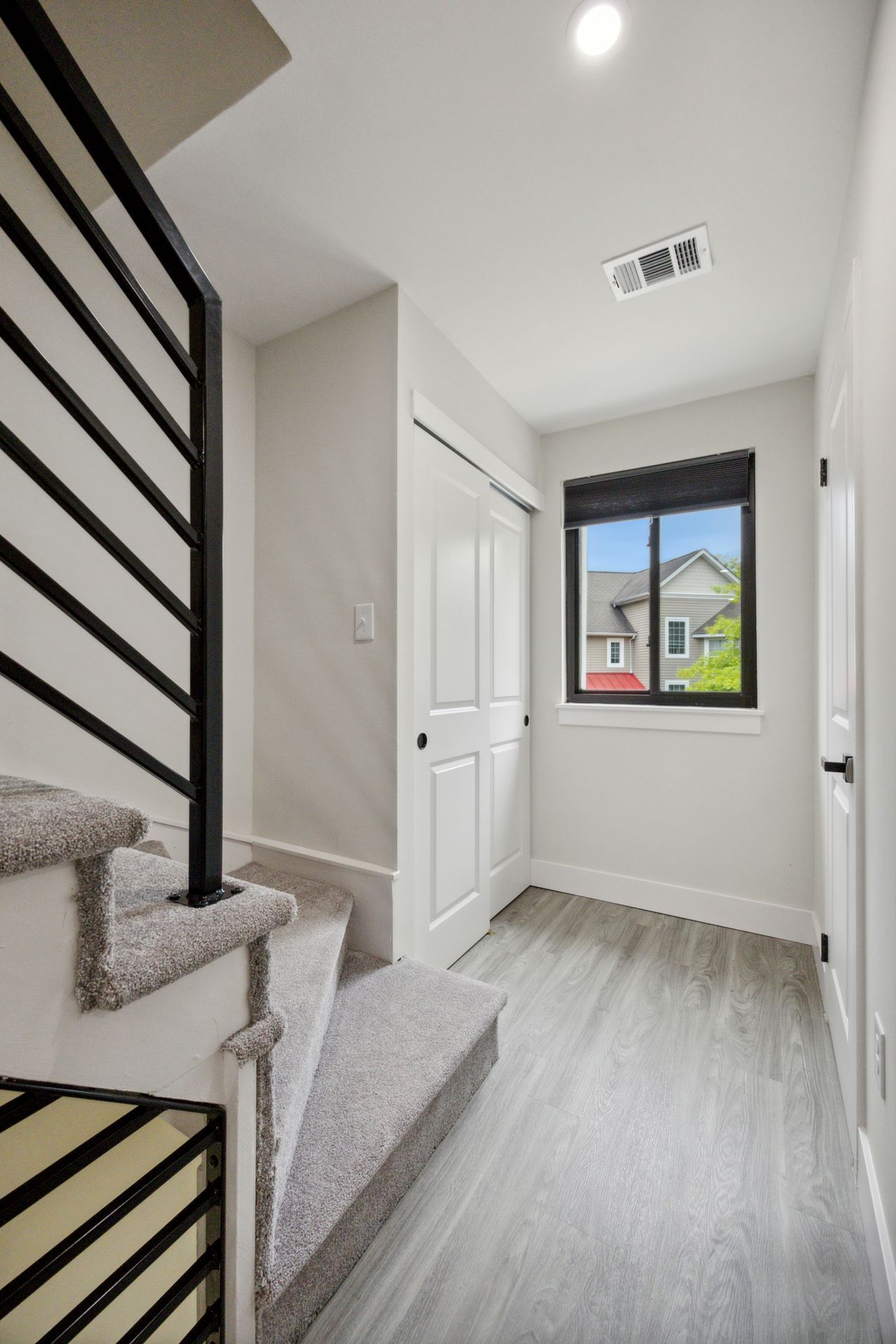 Staircase with gray carpet leading to a hallway with a closet, window, and black door.