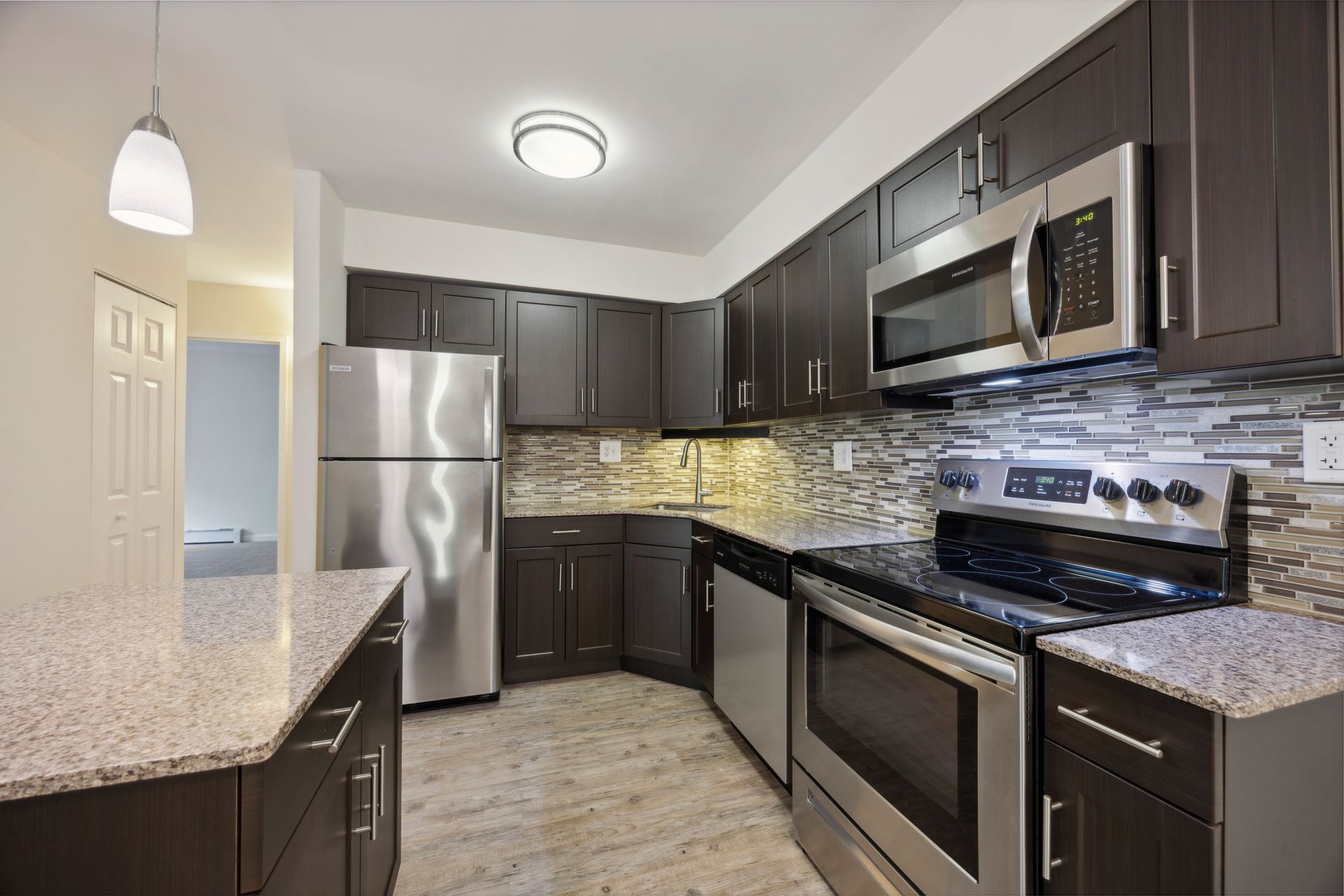 Kitchen with dark brown cabinets, stainless steel appliances, and gray speckled countertops.