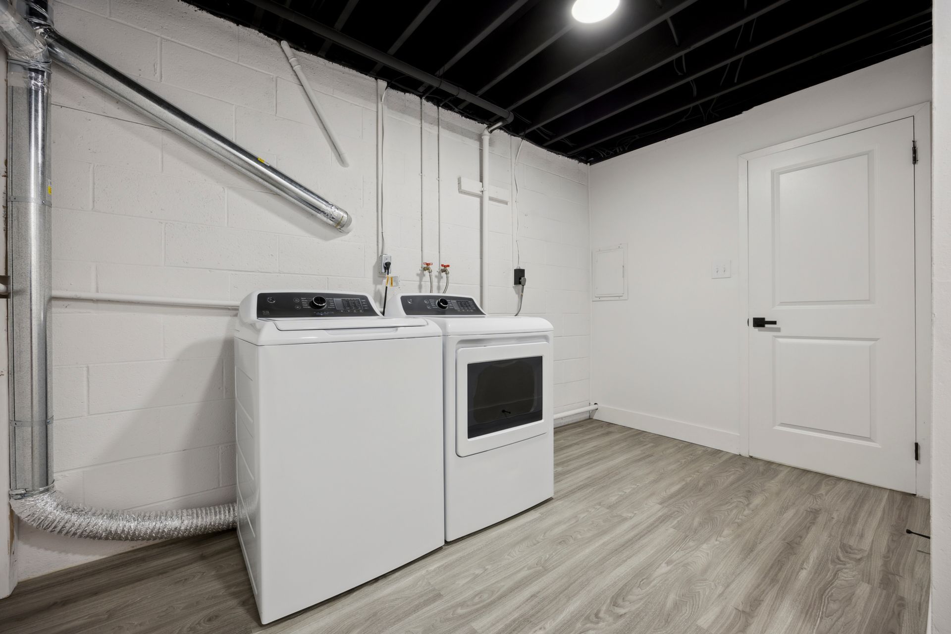White washer and dryer in a basement laundry room with gray flooring, white walls, and a black ceiling.