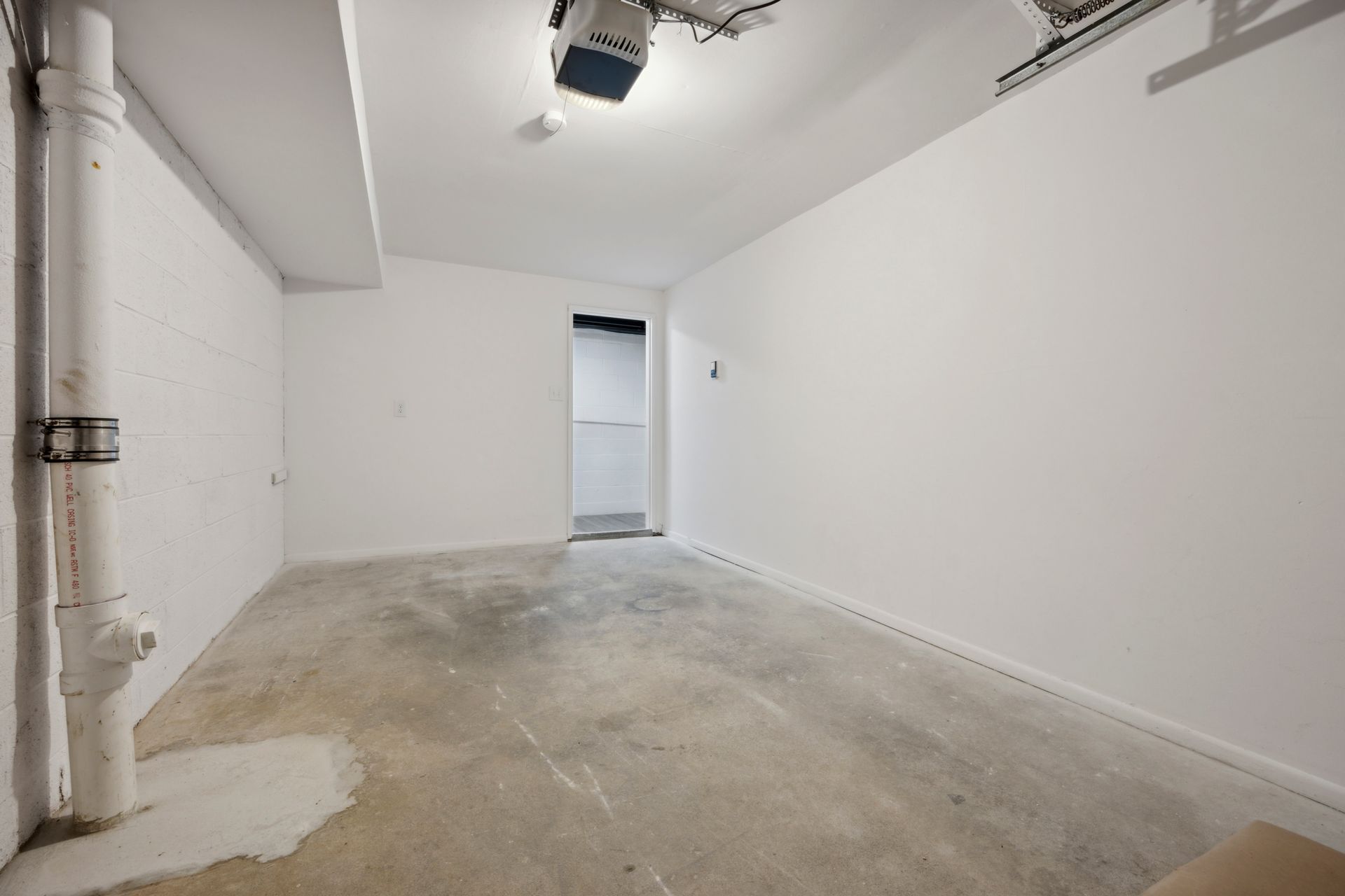 Empty, white-walled room with concrete floor, plumbing pipe, open doorway.