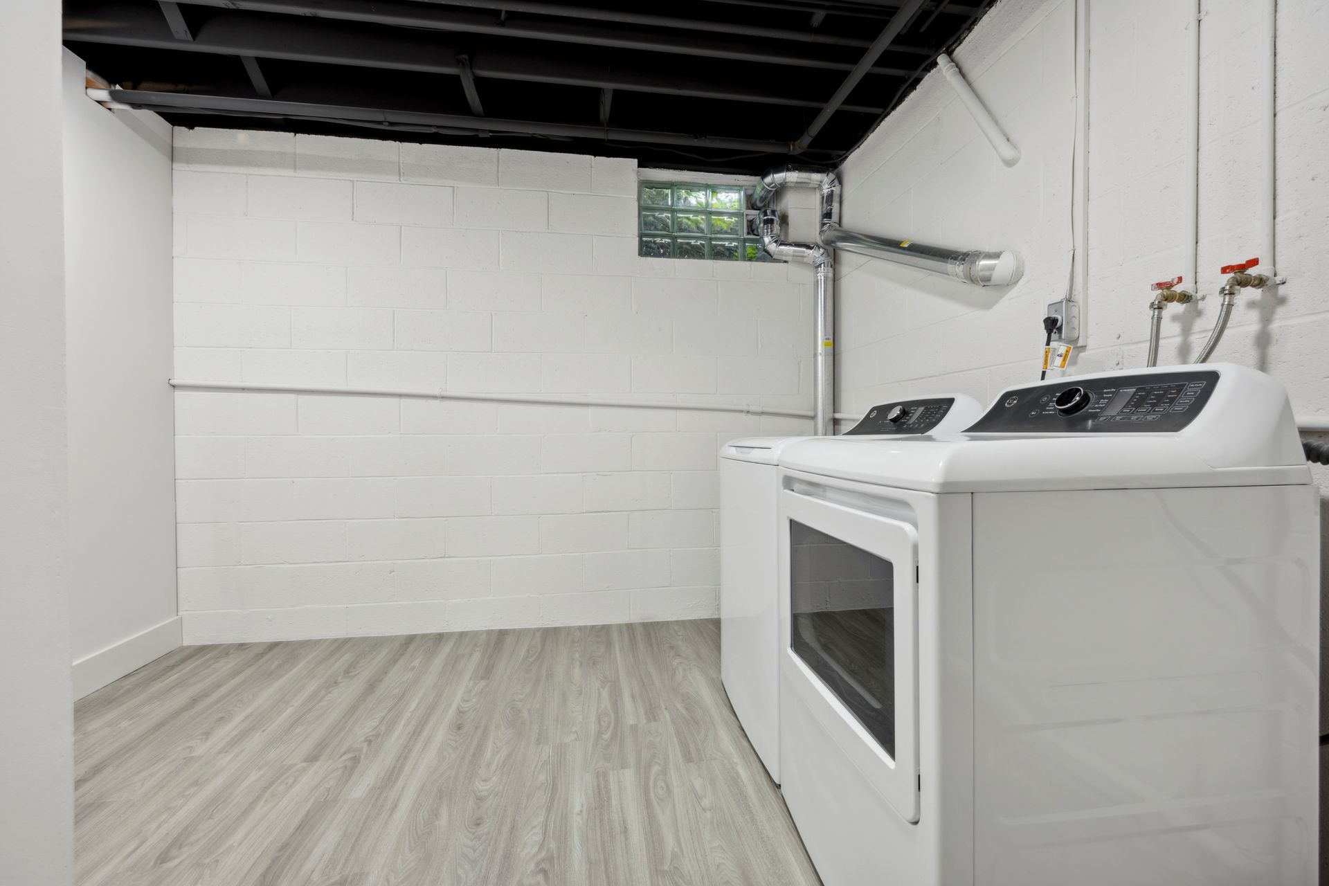 Laundry room with white appliances, painted cinder block walls, and gray flooring.