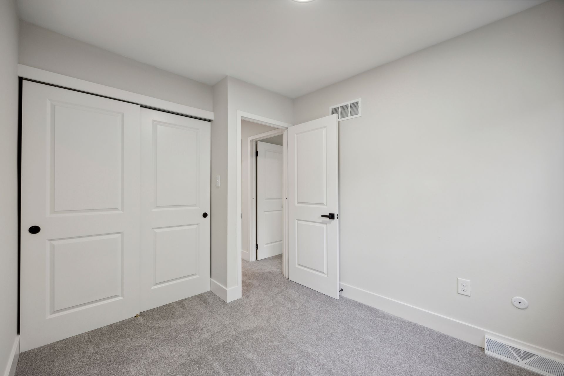 Empty bedroom with gray carpet, white walls, closet, and open door to hallway.