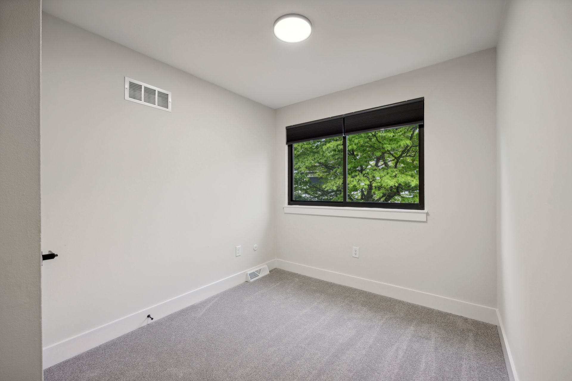 Empty bedroom with gray walls, carpet, window, and ceiling light.