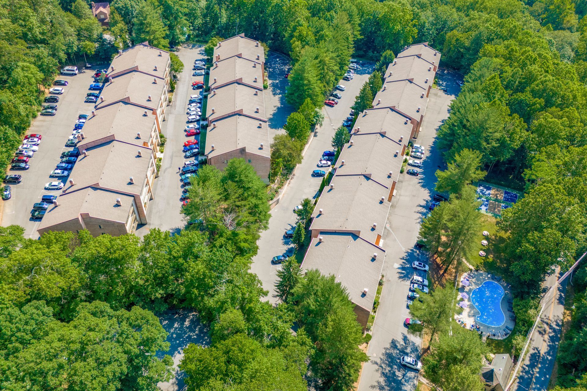 Aerial view of apartment complex with parking lots surrounded by trees.