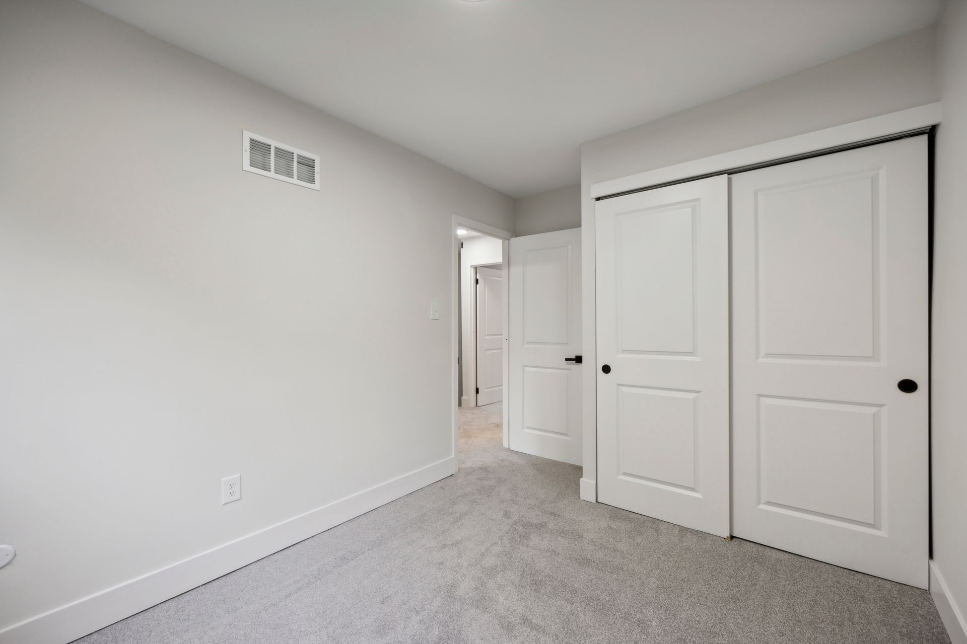 Empty bedroom with gray carpet, white walls, and closet doors.