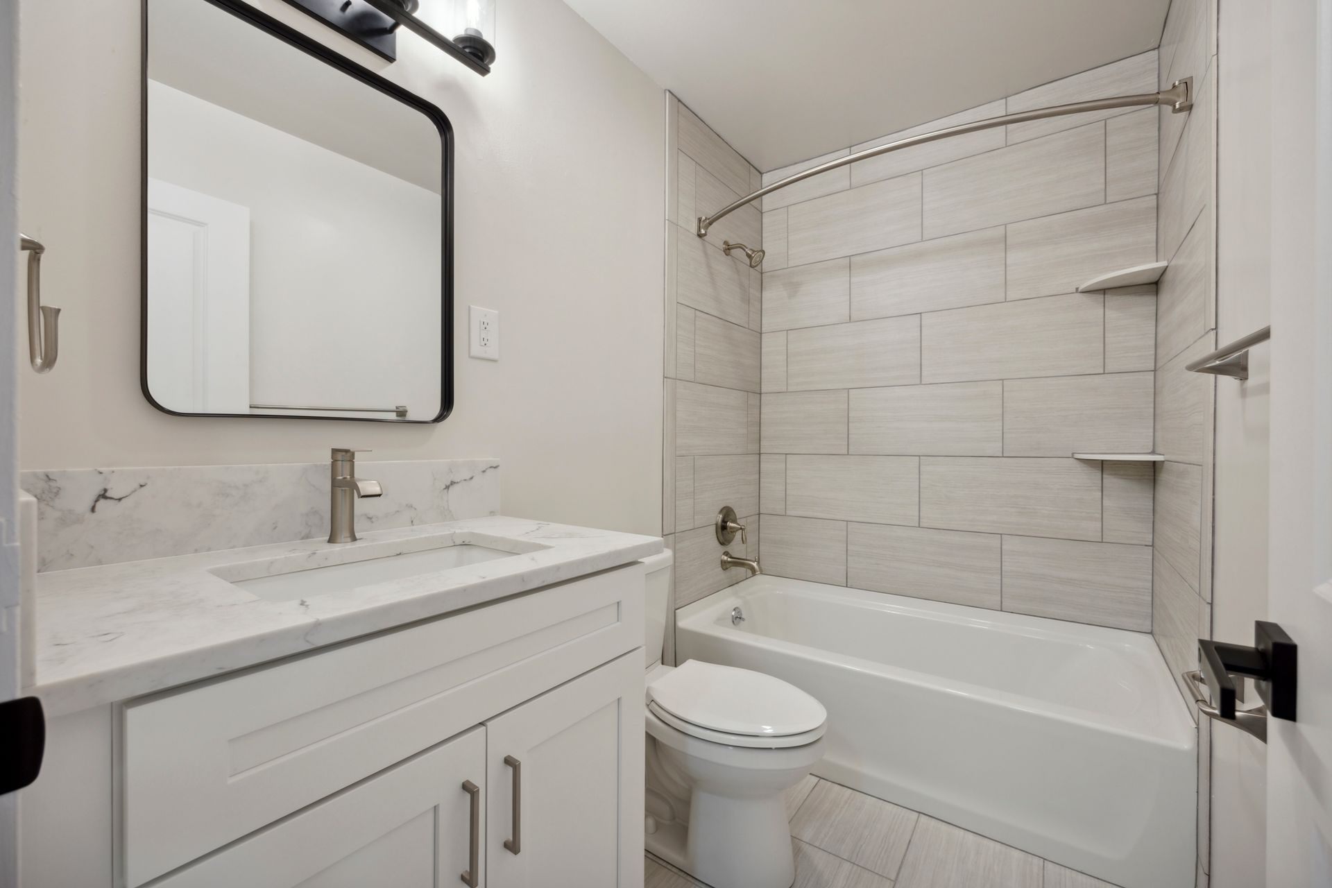 Modern white bathroom with vanity, toilet, and bathtub with tile surround.