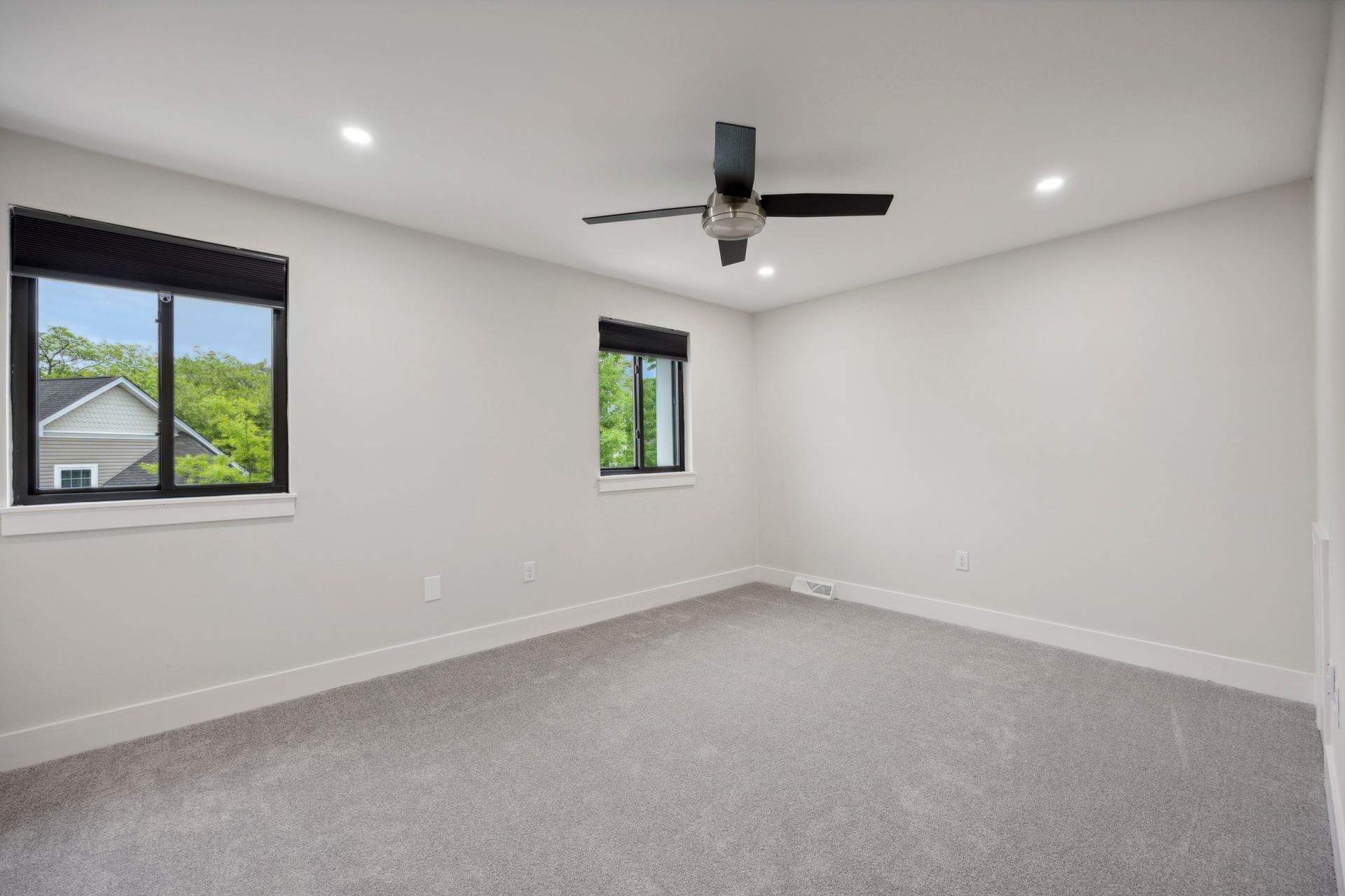 Empty bedroom with grey carpet, white walls, black windows and ceiling fan.