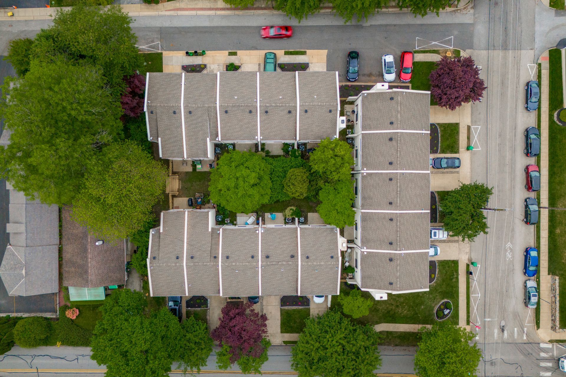 Aerial view of townhouses with trees, parked cars, and a street.