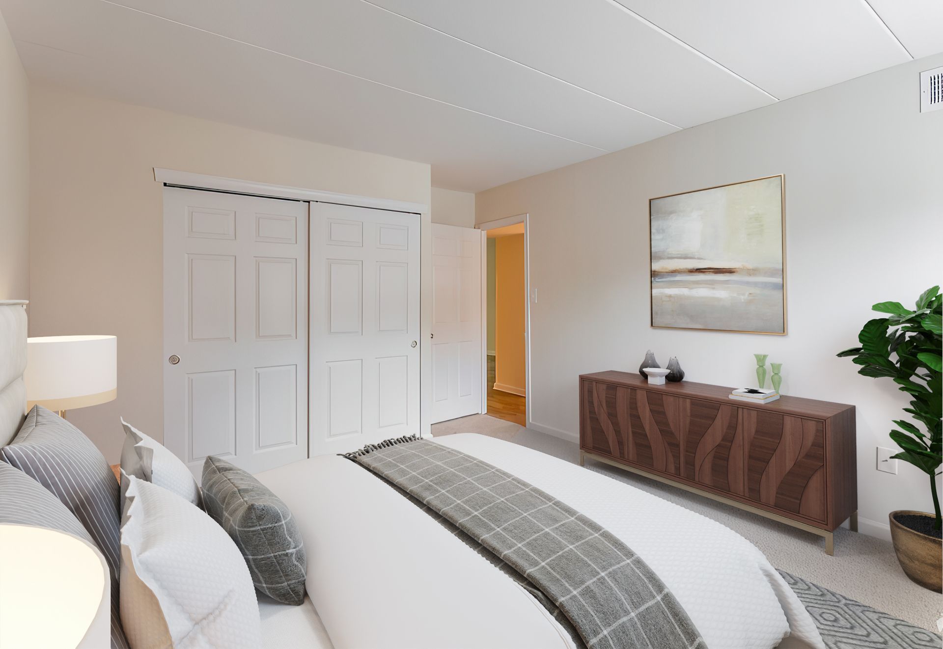 Bedroom with bed, dresser, art, and plant. White walls and closet doors, beige carpet.