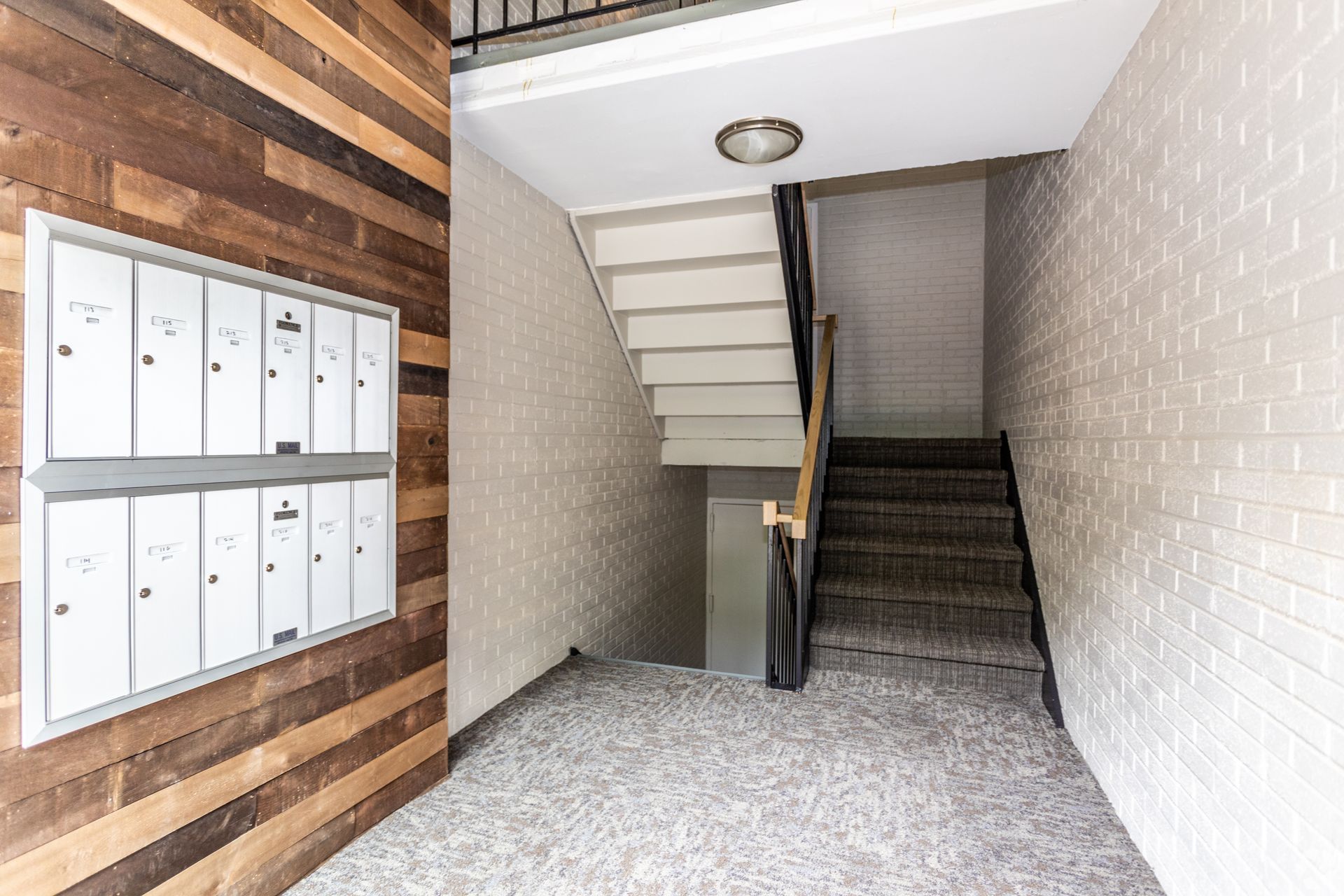 Apartment building entrance with mailboxes on wood paneling, stairs with carpet and handrail.