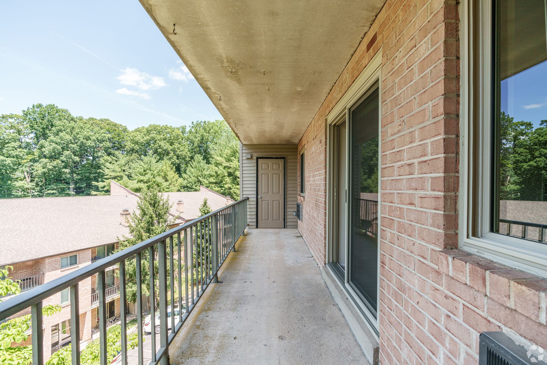 Balcony overlooking trees, with brick wall, sliding glass door, and metal railing.