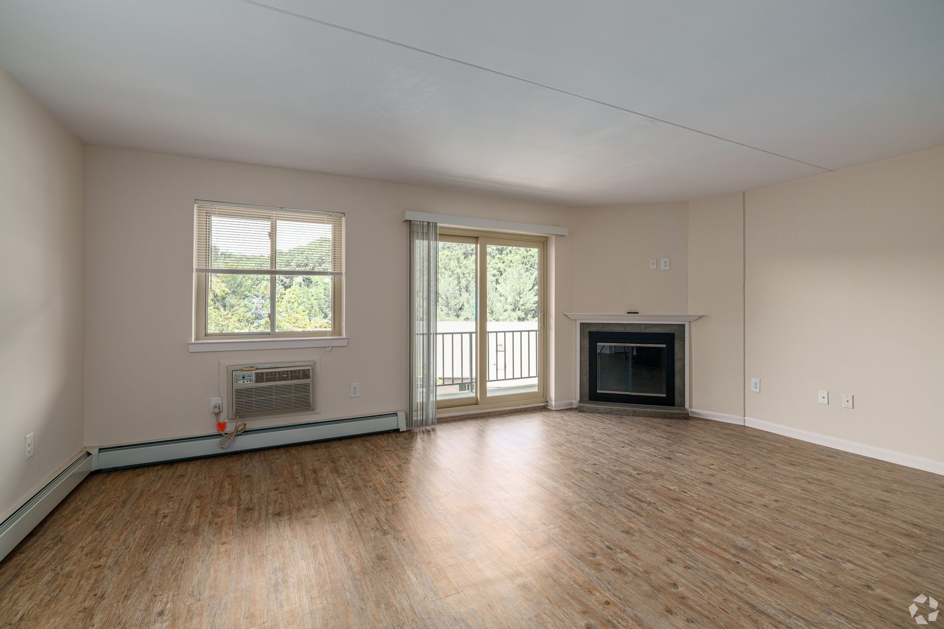 Empty apartment living room with wood flooring, fireplace, and balcony access.